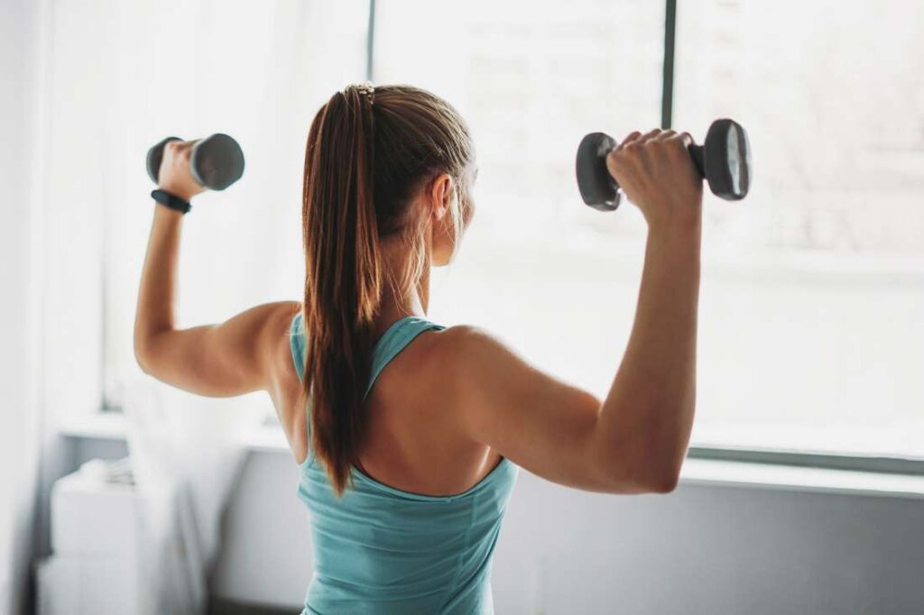 Woman lifts dumbell weights into shoulder press.