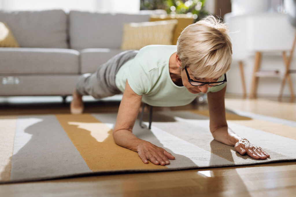 An older woman doing Pilates at home on a mat.